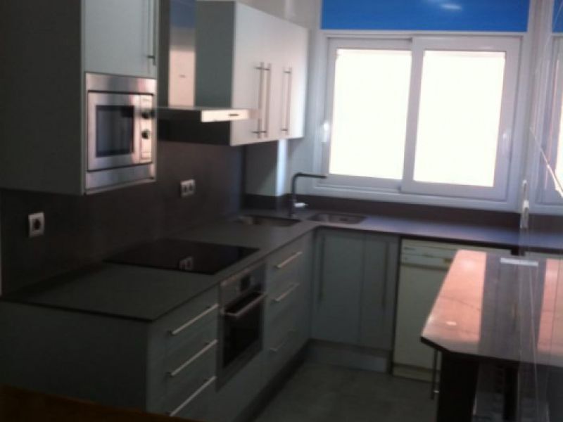 Reforma de cuina amb mobles blancs, blau a la paret i taulell fosc amb taula a la dreta