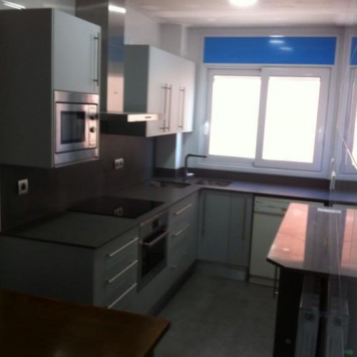 Reforma de cocina con muebles blancos, azul en la pared  y encimera oscura con mesa a la derecha