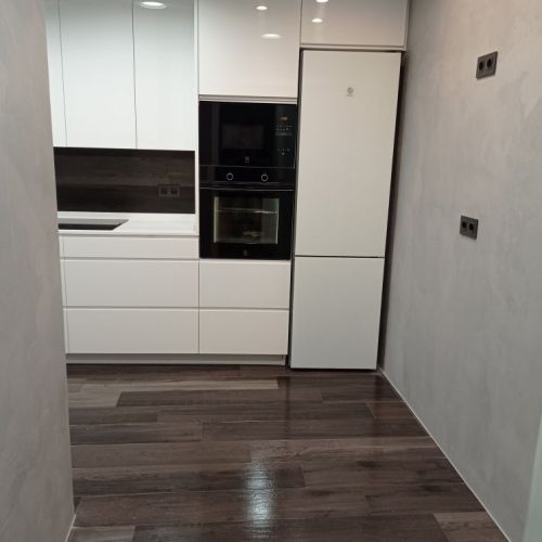 Cocina con muebles de color blanco y frontal de pared en negro y suelo marrón