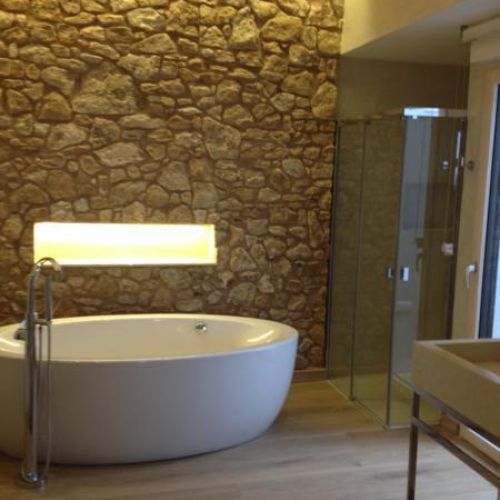 Bañera exenta con pared de piedra y plato de ducha a la derecha